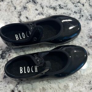 Bloch children's patent blk tap shoe, w/ a single strap & button snap closure.